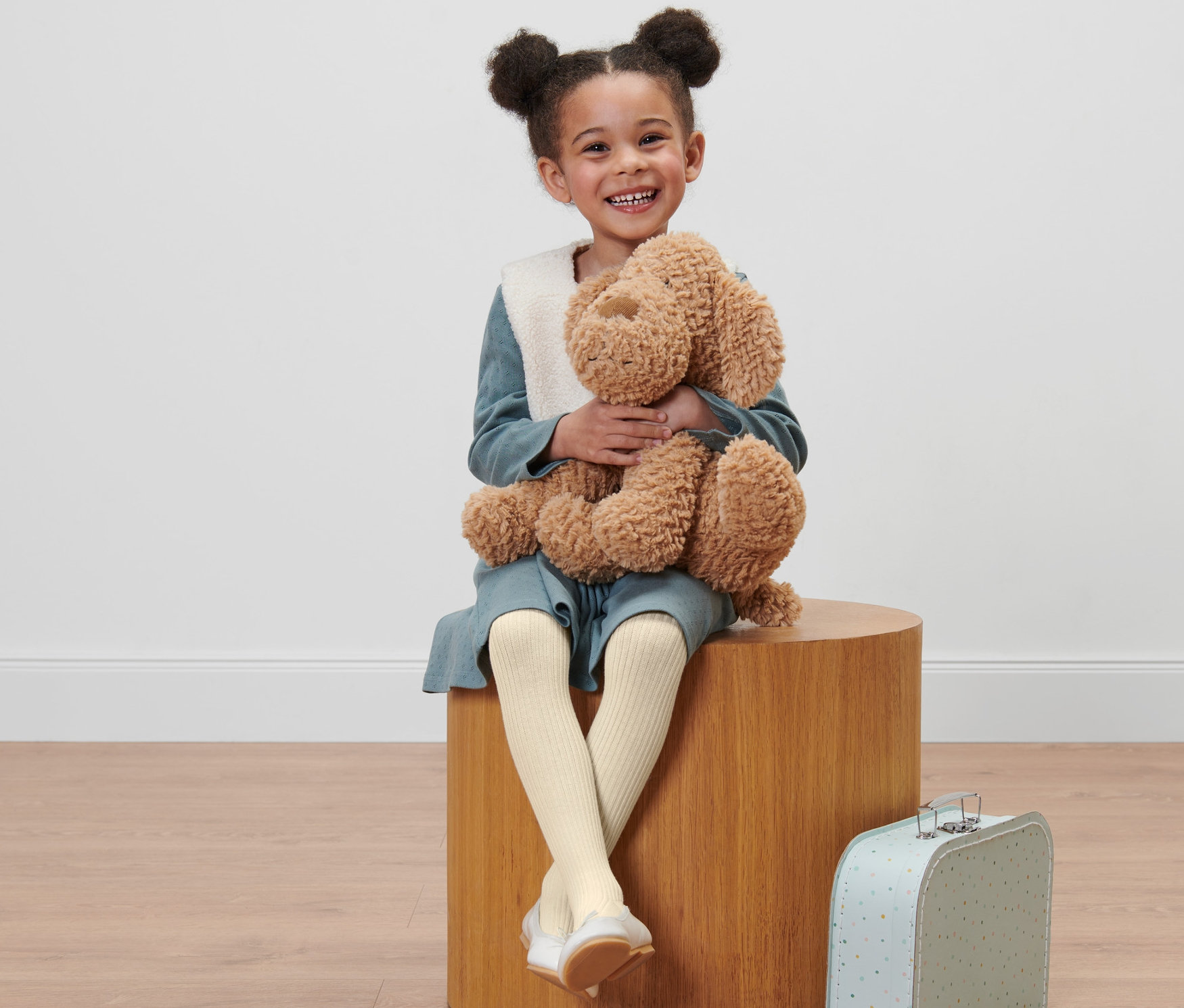 Gülümseyen kız çocuğu oyuncak ayısıyla oturuyor ve 2 Adet Çocuk Külotlu Çorap, Tek Renk giyiyor.