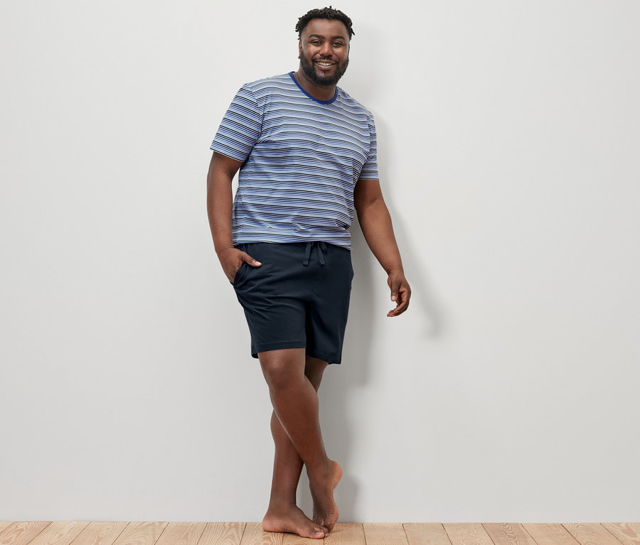 Adam yerde poz veriyor, üzerinde mavi-lacivert şortlu pijama takımı var.