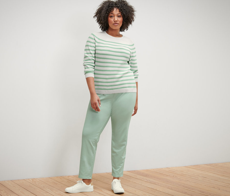 Kadın çizgili örgü kazak ve jogger pantolonla poz veriyor.