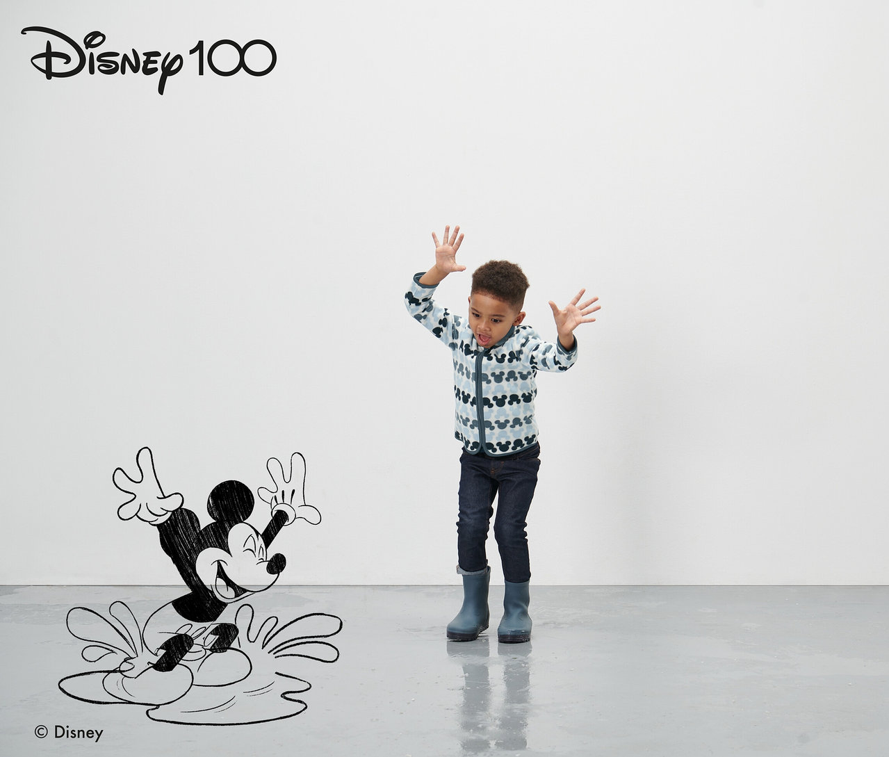 Bir çocuk çizgi film Mickey Mouse figürünün önünde duruyor ve ellerini sallıyor. Mavi Küçük Çocuk Polar Ceket »Micky« giyiyor.