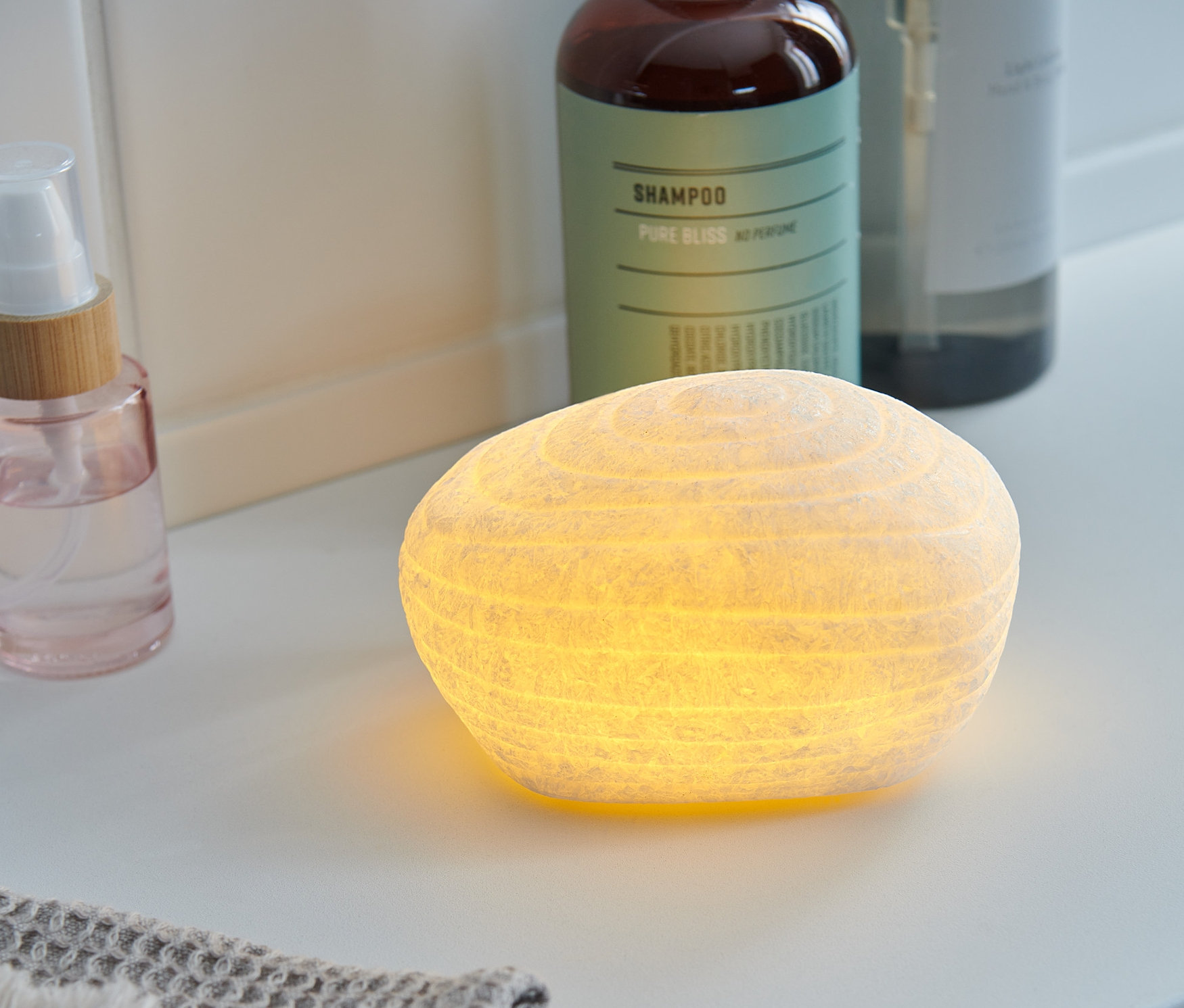 Beyaz bir banyo rafında yanan bir LED Dekoratif Taş duruyor.