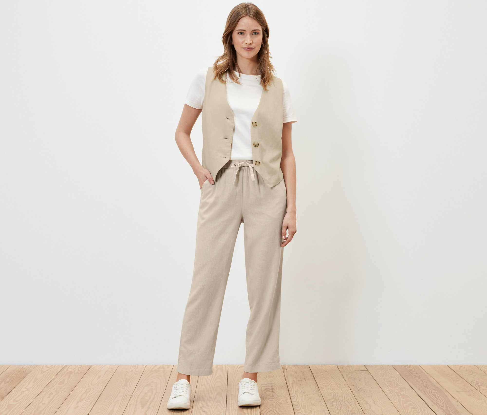 Kadın kum rengi keten pantolon ve yelek ile poz veriyor.