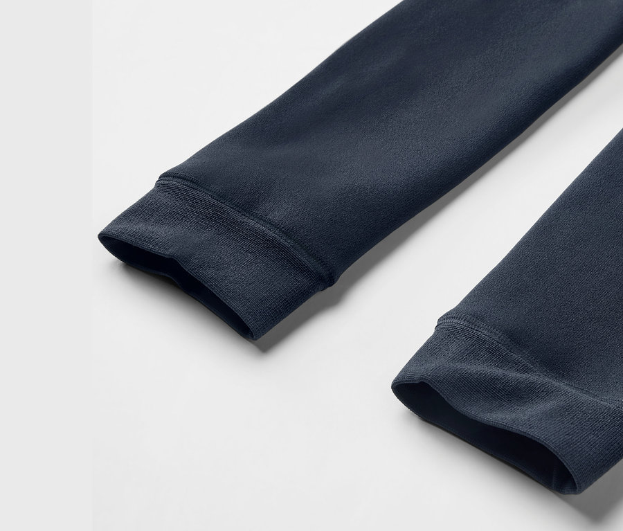 Beyaz bir arka plan üzerinde, nervürlü manşetlere sahip, lacivert bir sweatshirt'ün iki kolunun yakın çekim detayı.