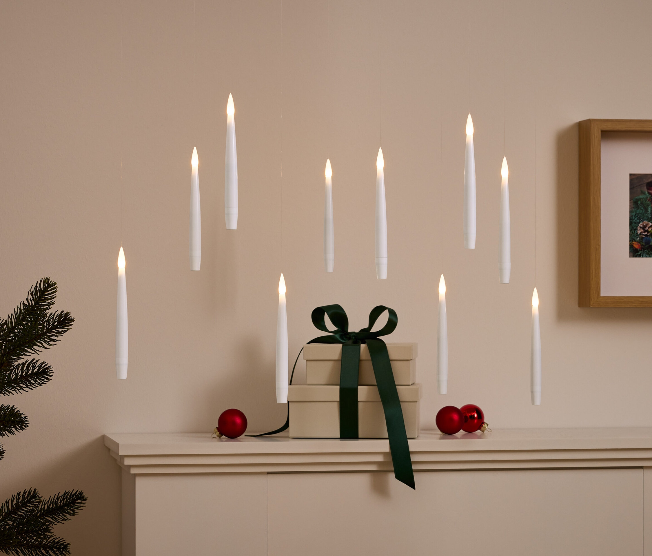 Tavandan sarkan beyaz mumlar, koyu yeşil kurdeleli bir hediye ve kırmızı süslemelerle dekoratif düzenleme.