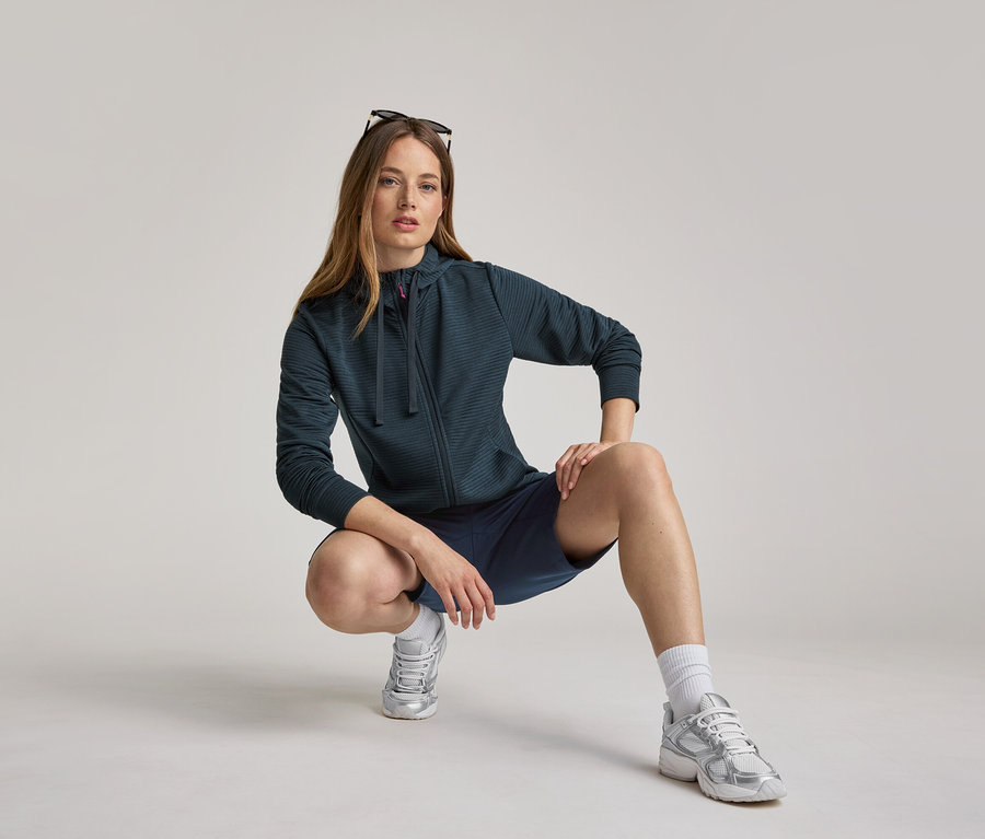 Kadın lacivert kapüşonlu ceket ve şortla çömeliyor. Kapüşonlu ceket lacivert.