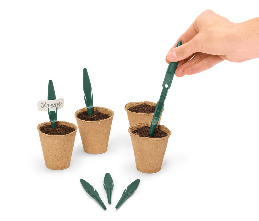 Bir el, kahverengi bir saksının içine yeşil bir tohum çubuğu yerleştiriyor, etrafı diğer saksılar ve tohum çubuklarıyla çevrili.