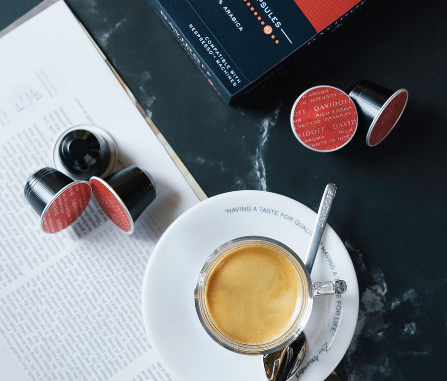 DAVIDOFF CAFÉ Rich Aroma paketinin ve kahve kapsüllerinin yanında kaşıklı fincan içinde espresso.