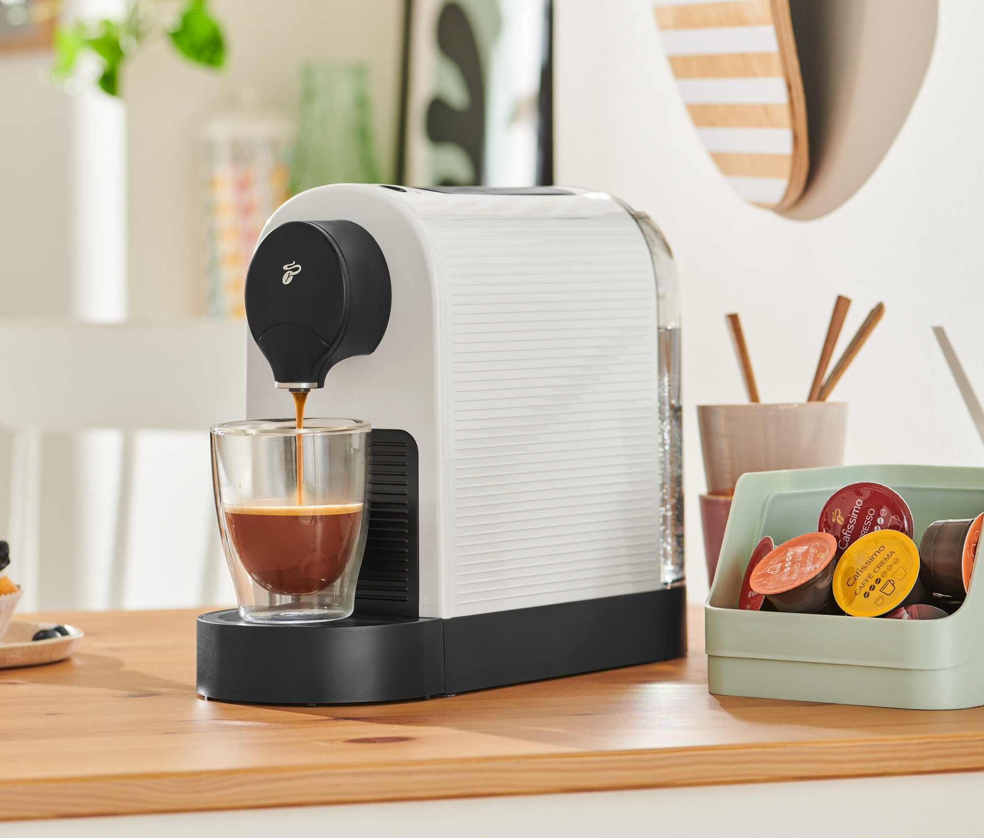 Cafissimo Pure+, Beyaz kahve makinesi bir bardağa kahve dolduruyor. Arka planda bir cupcake var.