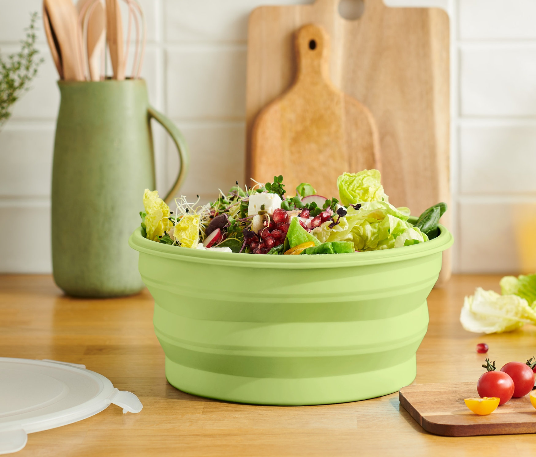 Ahşap bir kesme tahtası üzerinde salata dolu yeşil katlanabilir salata kasesi.