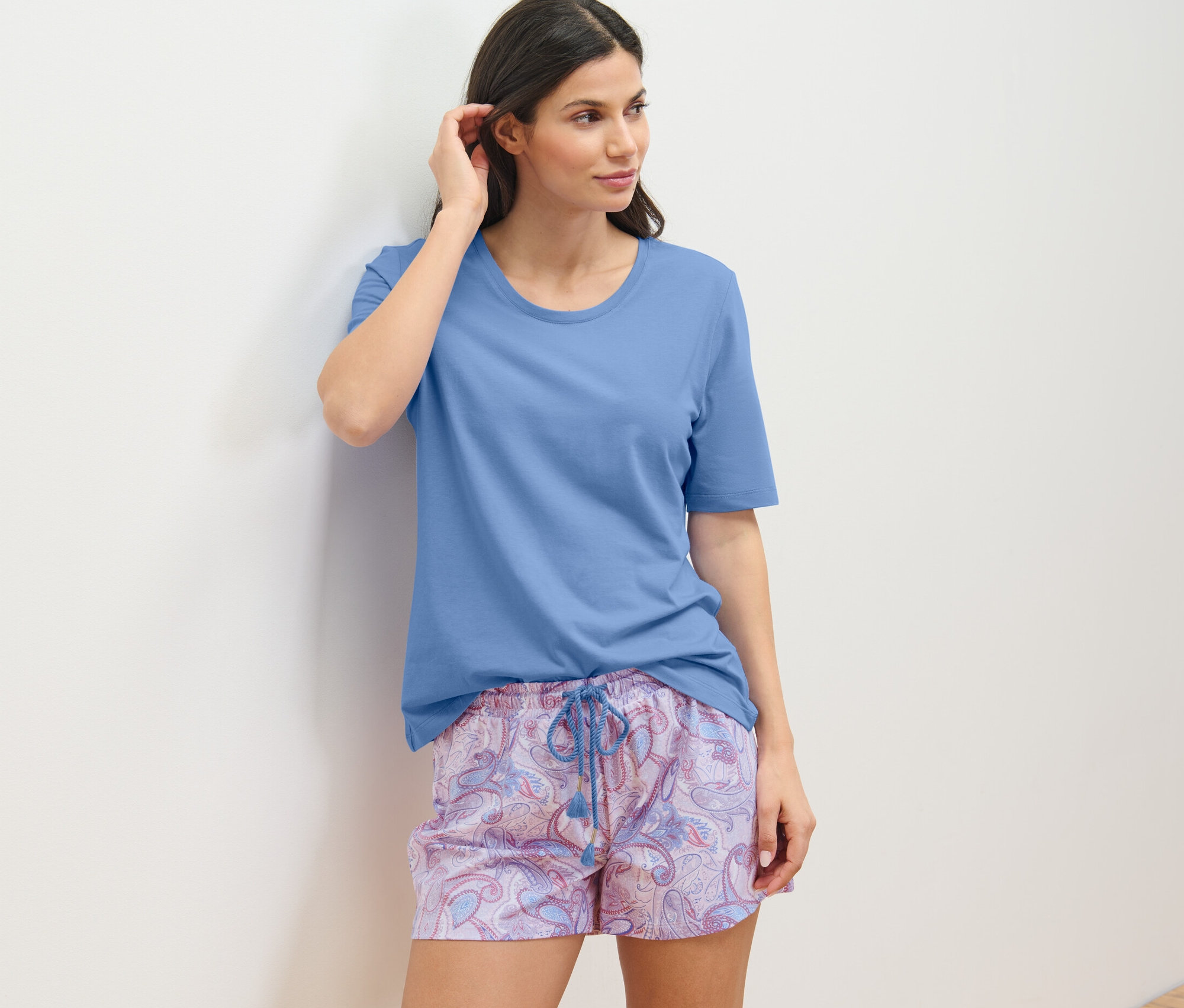 Duvara yaslanmış şortlu pijama takımı giyen kadın.