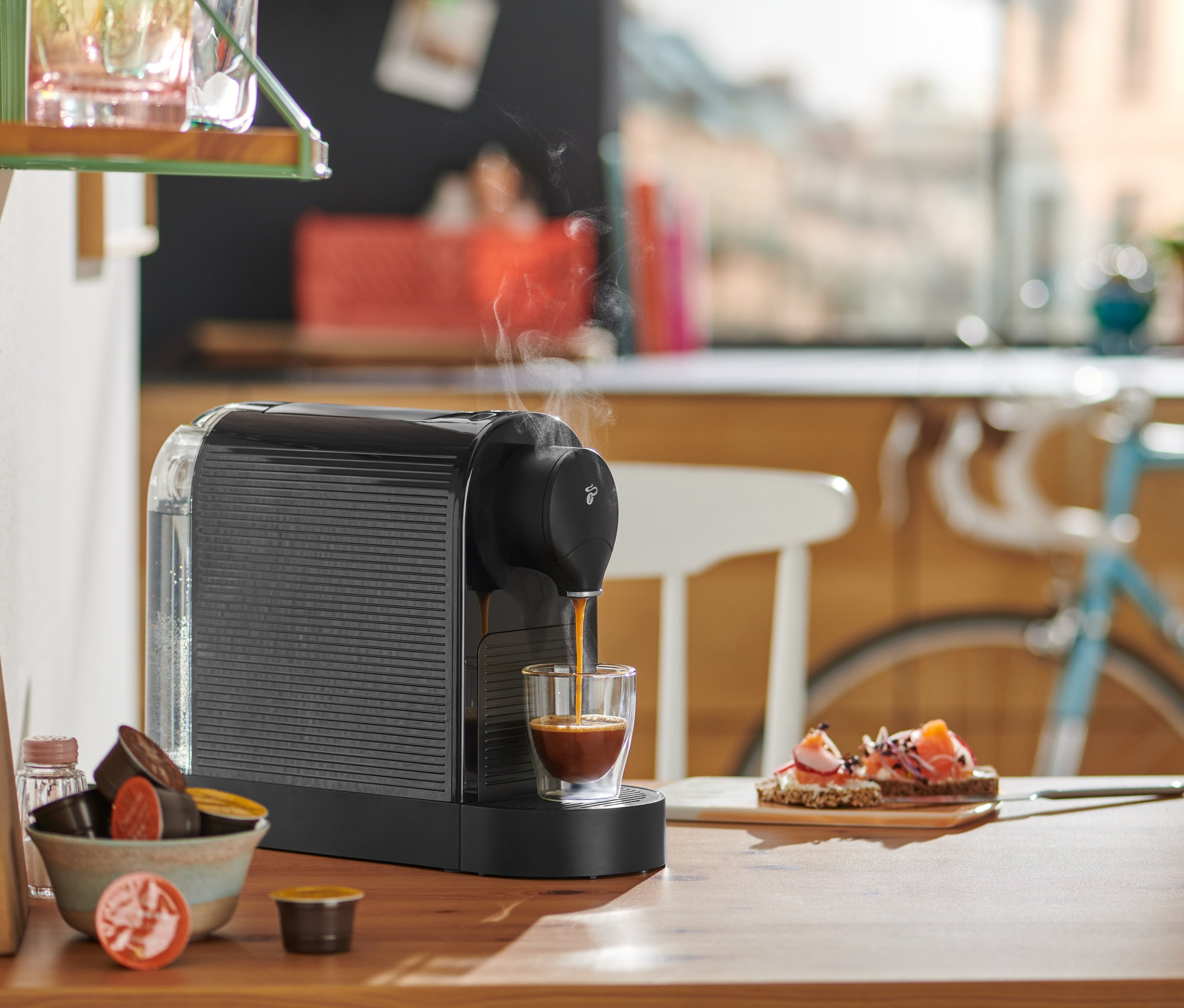 Siyah Cafissimo Pure+ kahve makinesi, ahşap bir masa üzerinde bir bardağa espresso hazırlıyor.