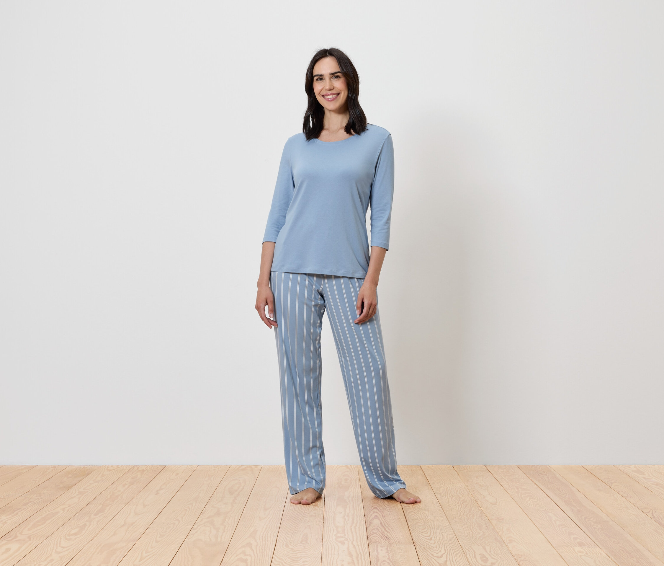 Kadın ayakta duruyor ve mavi, çizgili bir pijama giyiyor.