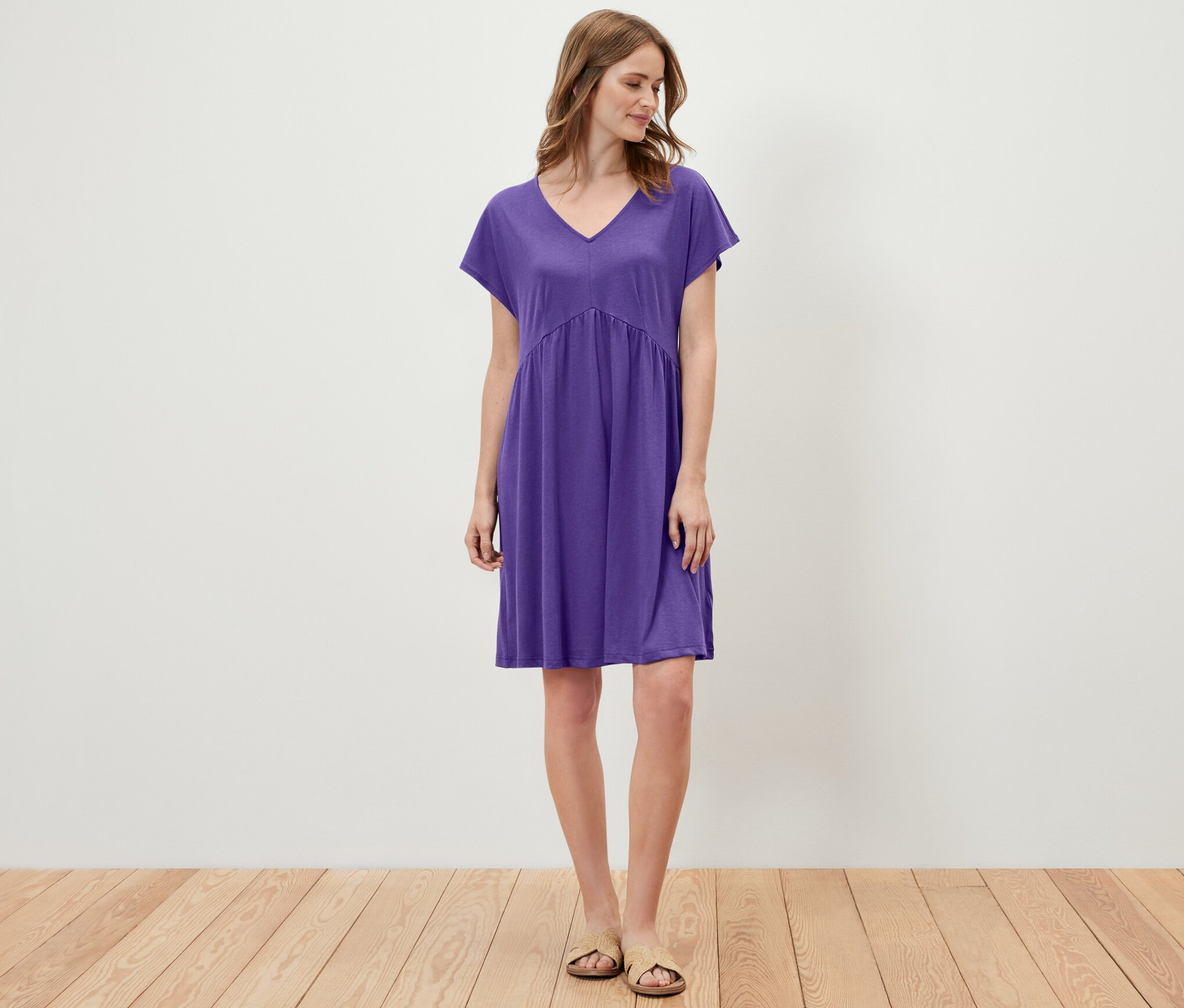 Bir kadın ayakta duruyor ve mor bir jarse elbise giyiyor.