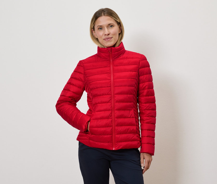 Kadın kırmızı kapitone ceketle poz veriyor.
