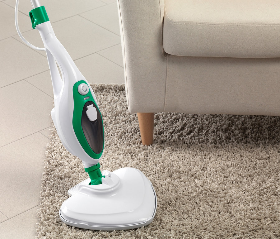 Bej halı üzerinde krem rengi koltuğun yanında çok fonksiyonlu buharlı paspas.