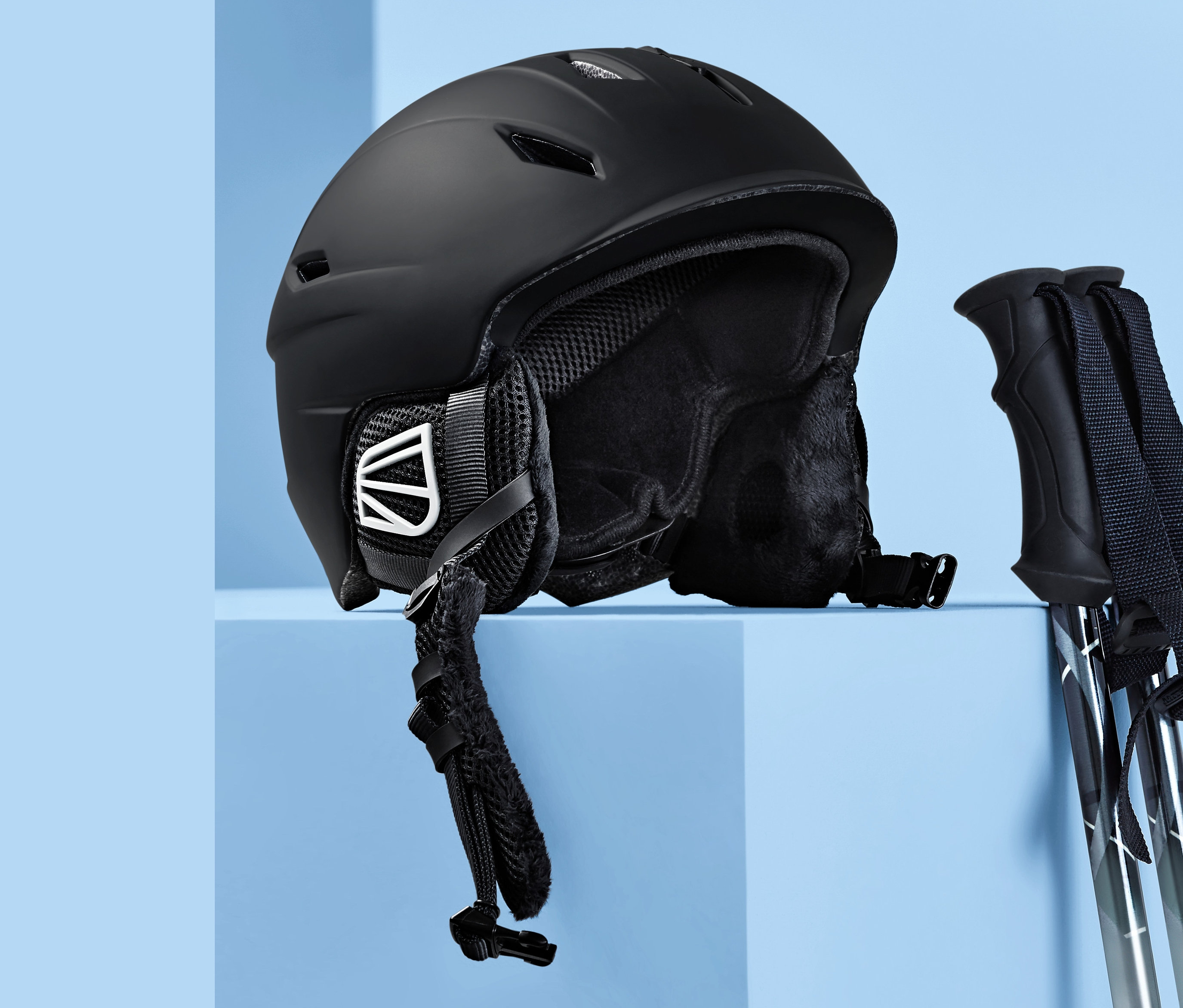 Mavi bir arka plan üzerinde siyah bir In-Mould Kayak ve Snowboard Kaskı ve kayak direkleri.