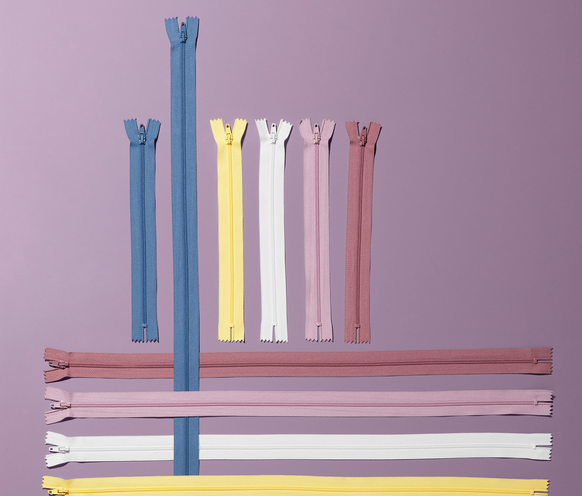 Mor arka planda farklı renk ve uzunluklarda 10 adet fermuar bulunmaktadır.