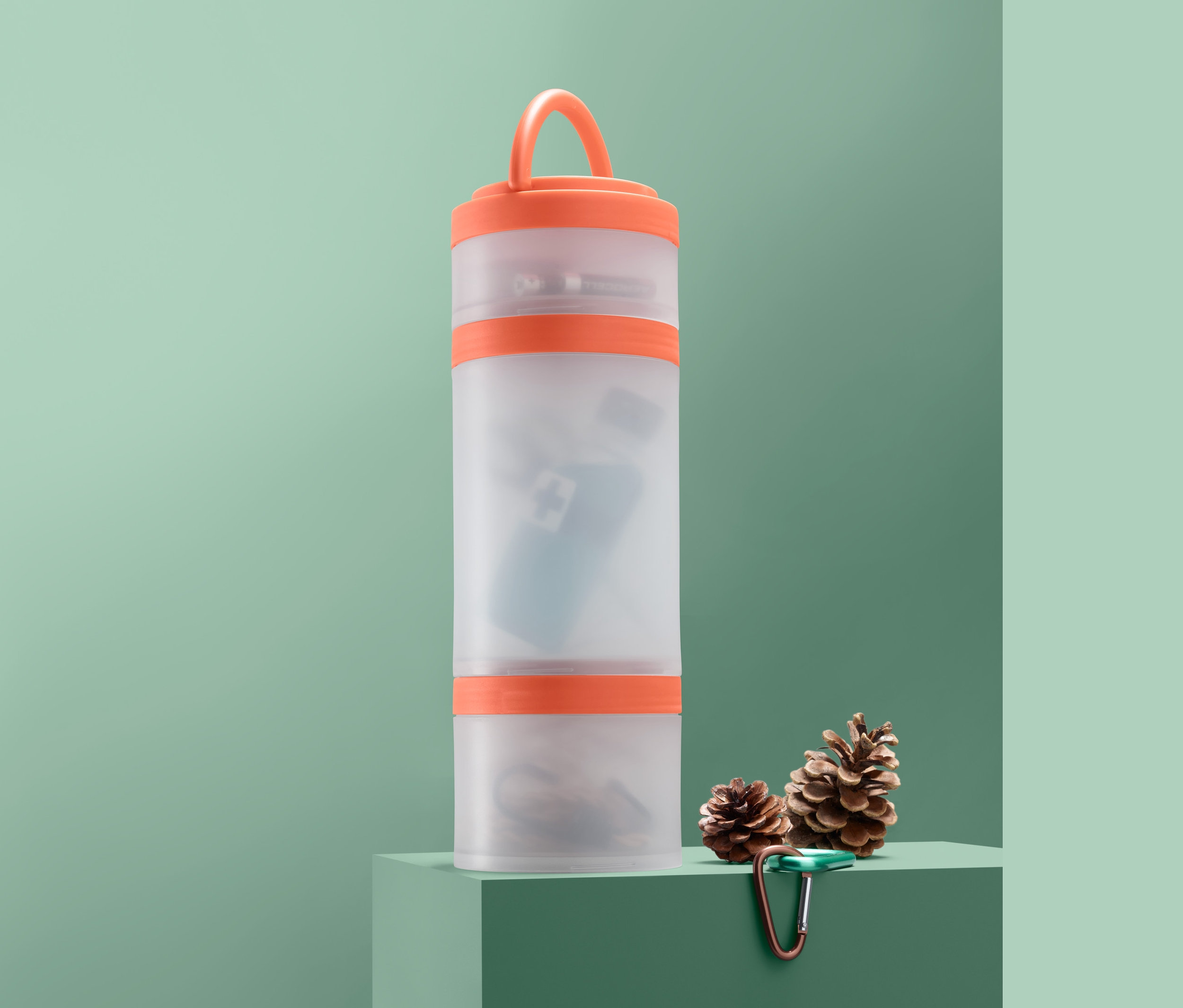 Çoklu Saklama Kutusu, iki çam kozalağı ve bir karabinanın yanında yeşil bir kaide üzerinde duruyor.