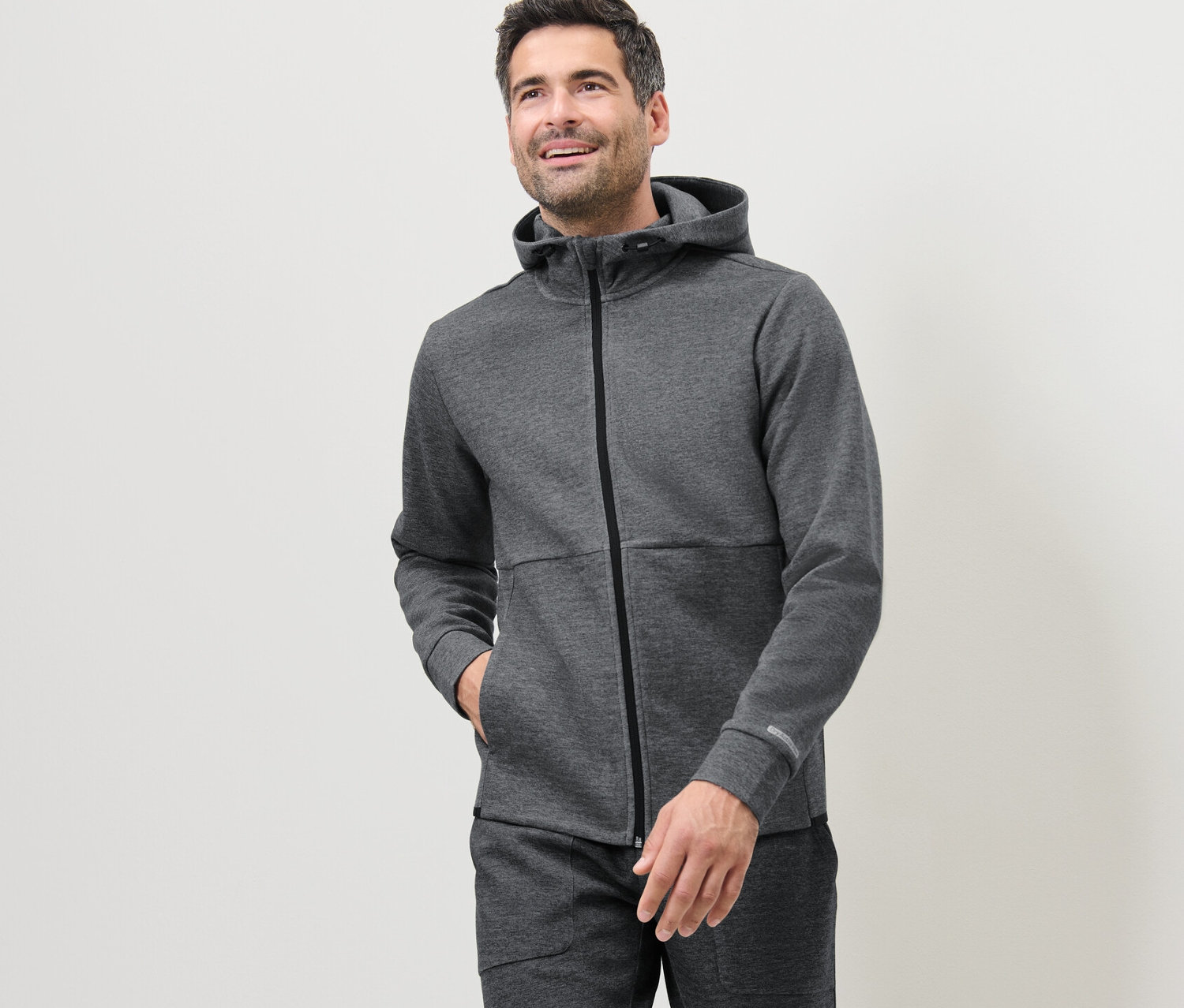 Adam, gri bir fonksiyonel sweat ceket giyiyor.