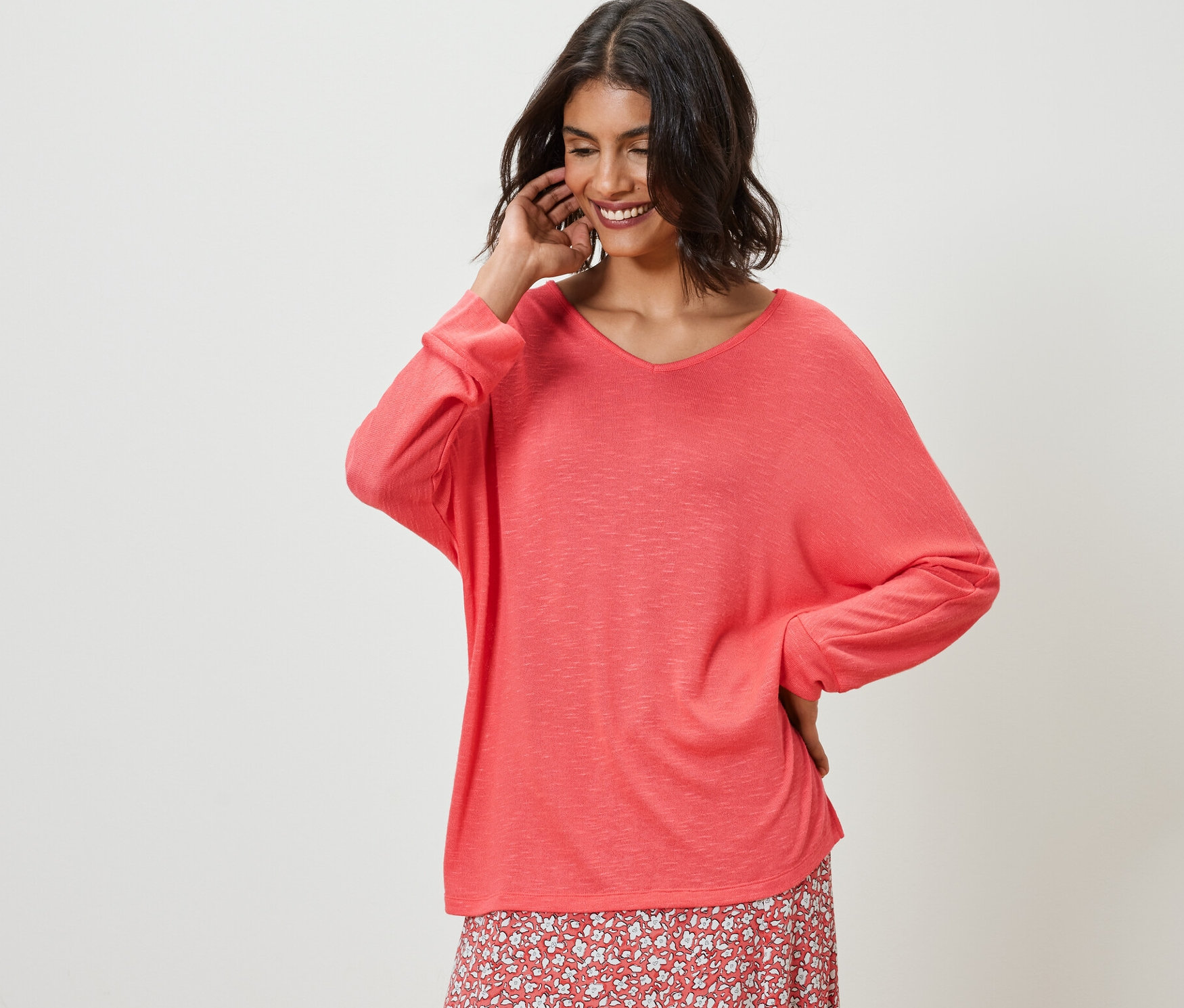 Kadın, mercan rengi yarasa kol bluzu ve çiçekli etekle poz veriyor.