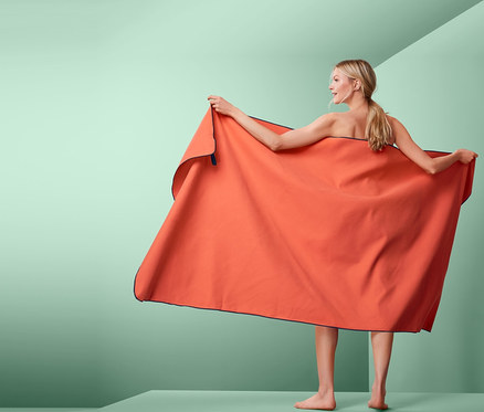 Kadın, turuncu renkli, yaklaşık 100 x 200 cm boyutlarında Outdoor XL Banyo Havlusu tutuyor.