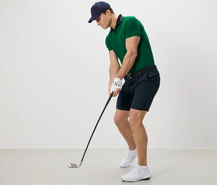 Yeşil polo tişört ve fonksiyonel şortlu adam golf oynuyor.