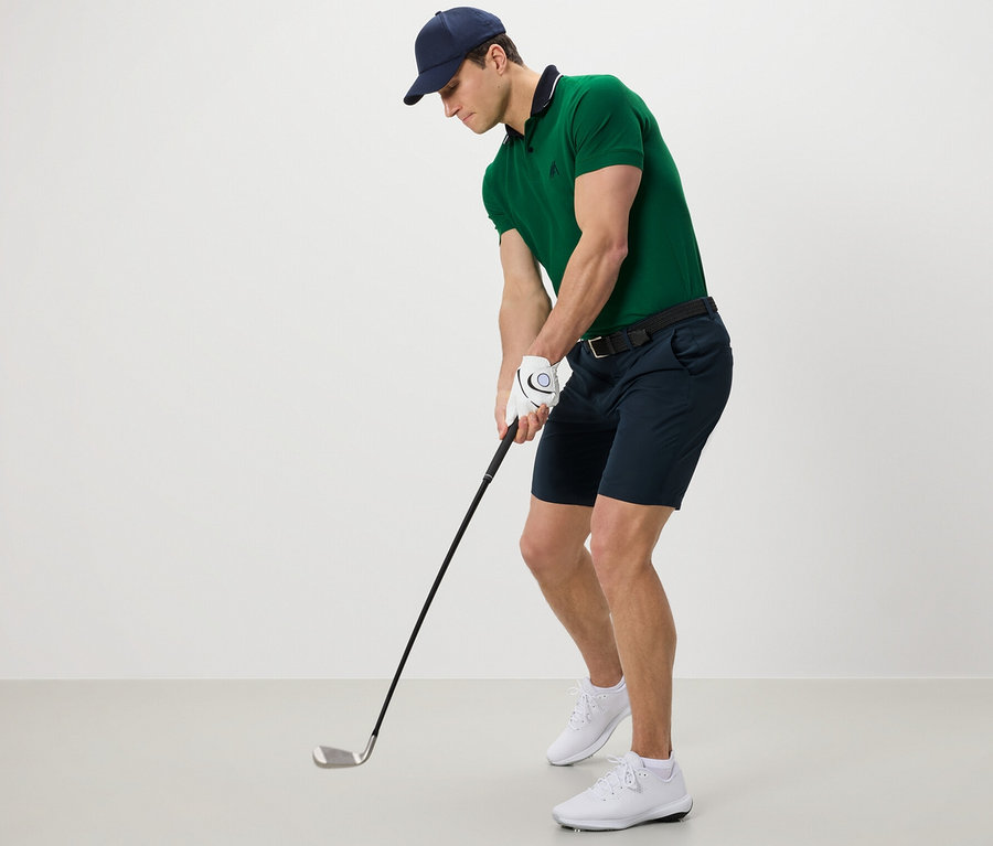 Yeşil polo tişört ve fonksiyonel şortlu adam golf oynuyor.