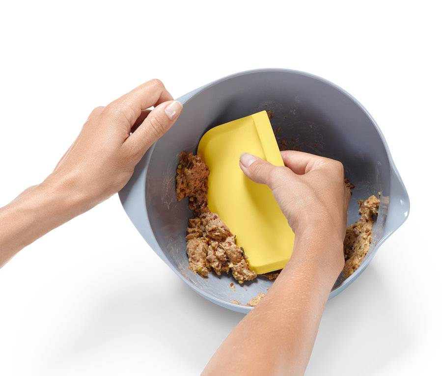 Bir çift el, sarı bir spatula ile bir kasede hamur karıştırıyor.