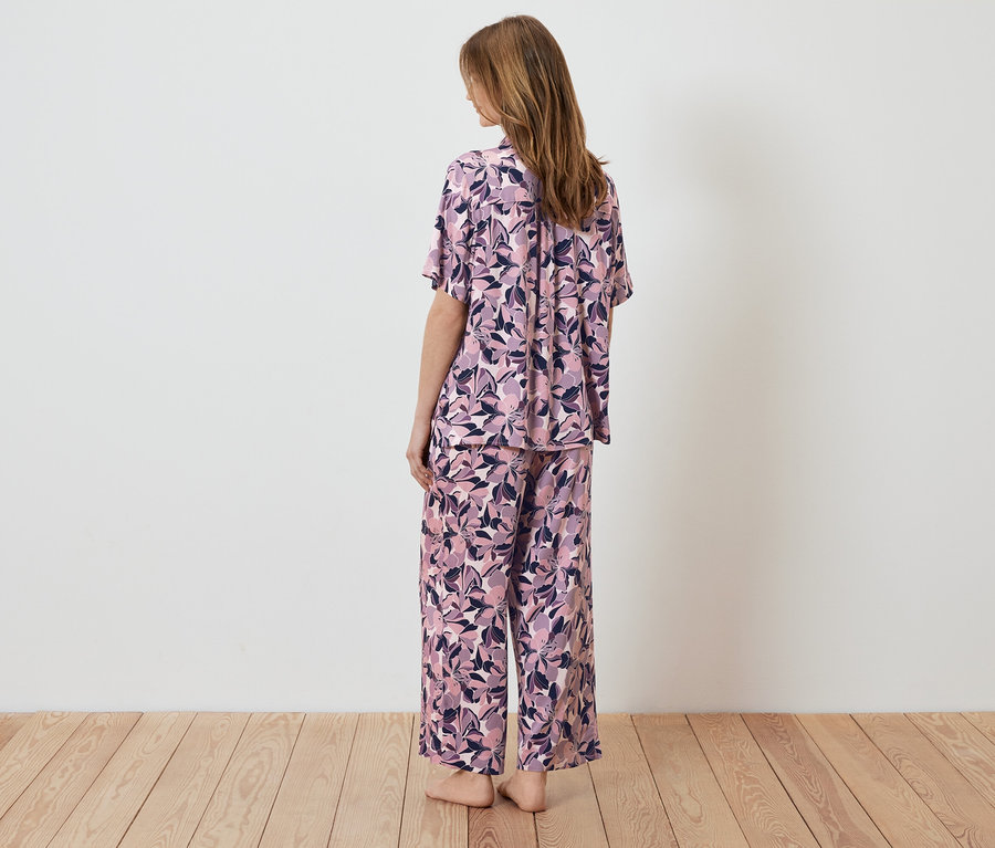 Kadın kameraya arkası dönük duruyor, çiçek desenli bir pijama giyiyor.