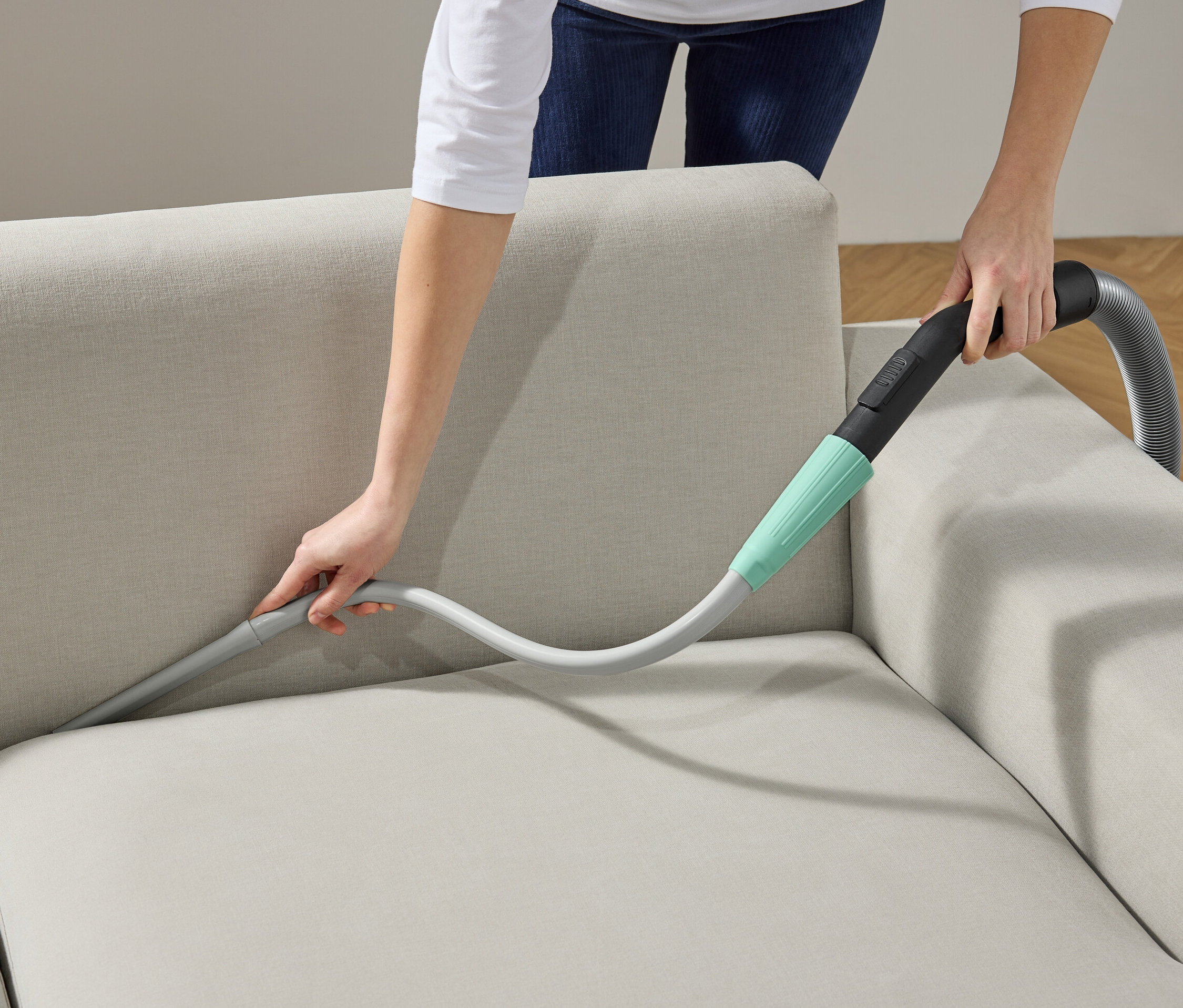 Kadın, elektrikli süpürge başlığıyla koltuğu temizliyor.