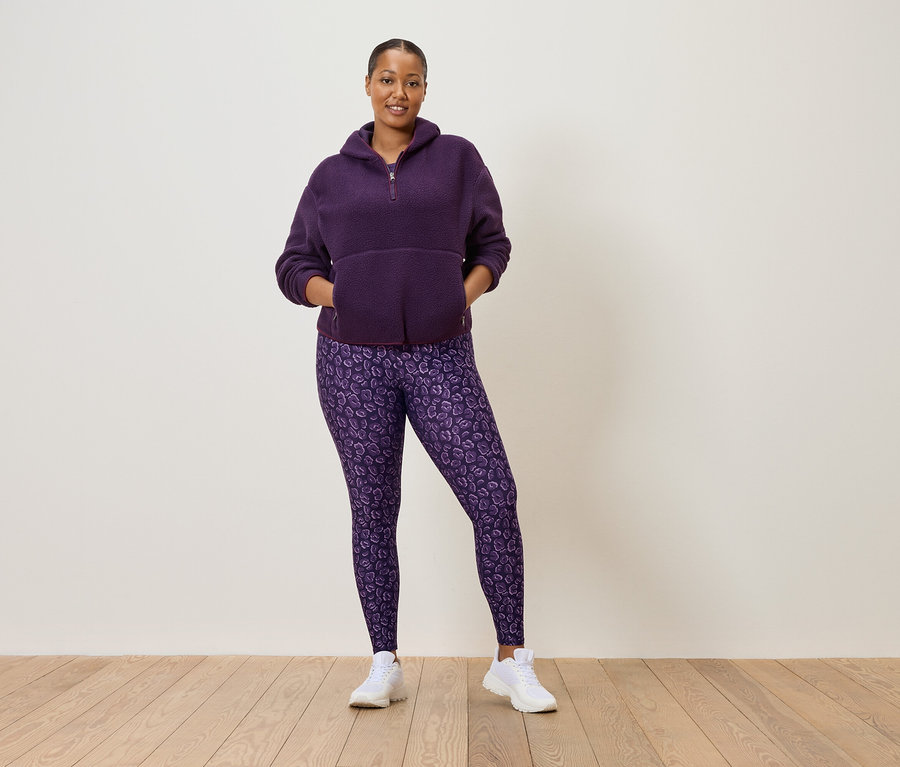 Mor renkli yarım fermuarlı polar kazak ve mor leopar desenli tayt giyen, beyaz spor ayakkabılı kadın.