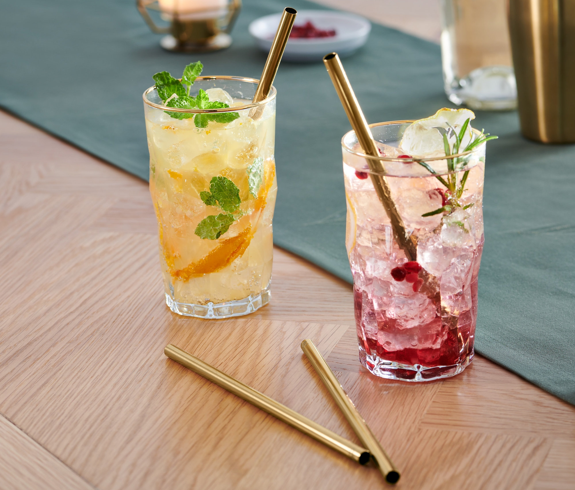 İki bardak içinde buz ve meyveler bulunan içecekler ve altın renkli 4 Adet Metal Pipet masanın üzerinde.