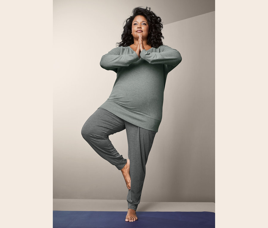 Gri Yoga Sweatshirt ve Yoga Pantolonu giyen kadın, mavi bir mat üzerinde ağaç duruşunda duruyor.