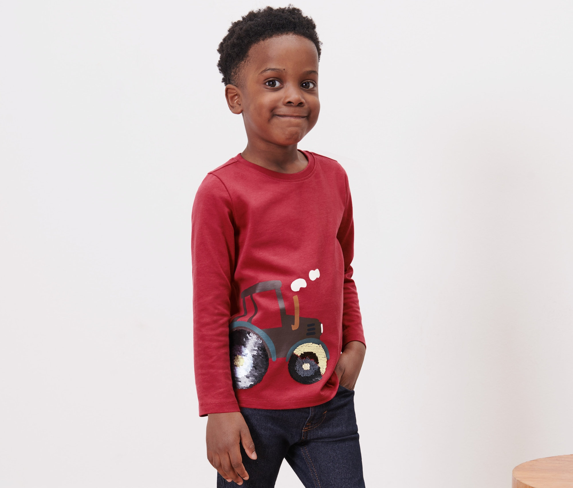 Traktör deseni olan kırmızı, uzun kollu tişört giyen bir erkek çocuk.