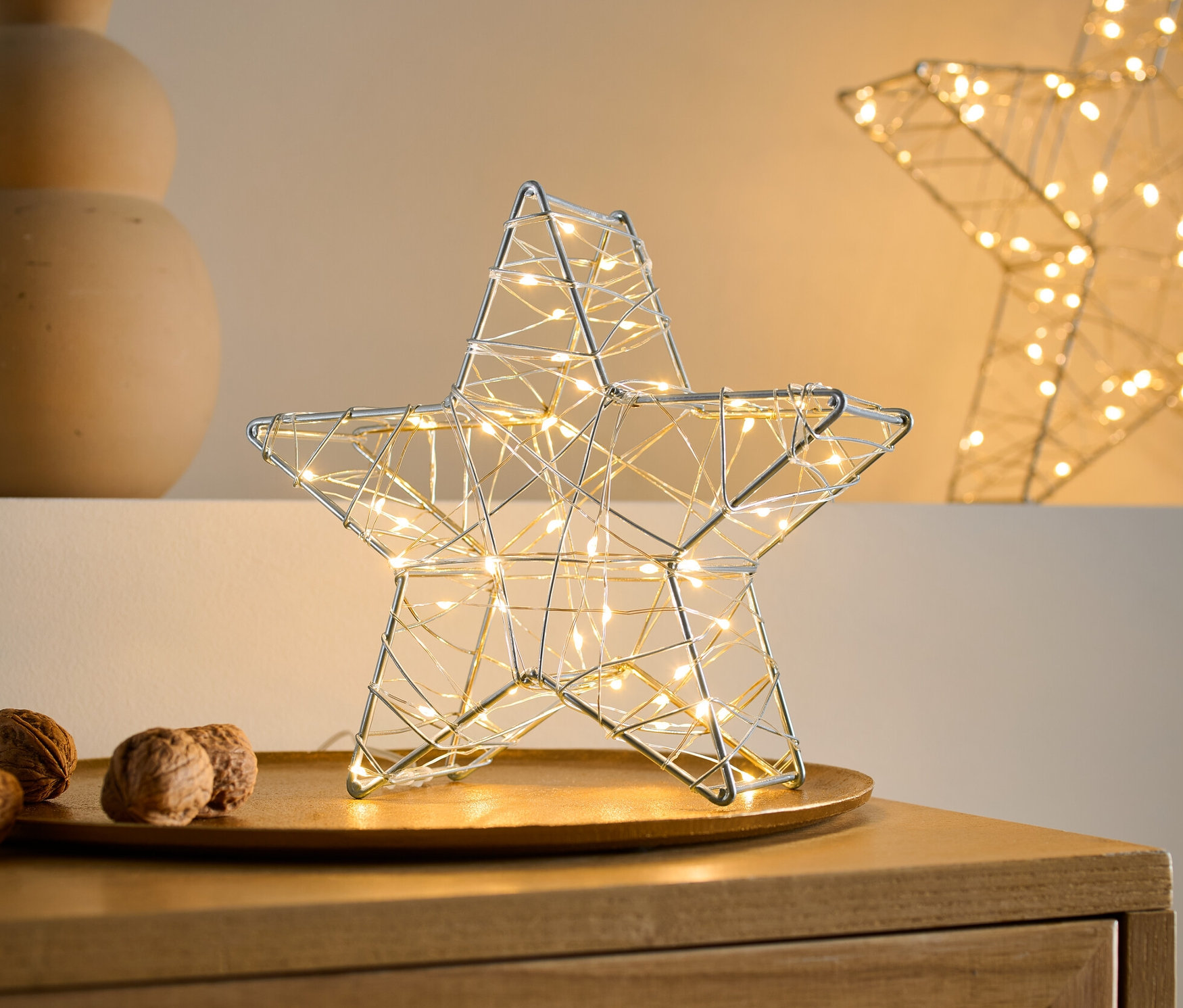 Tepside küçük bir LED'li dekoratif yıldız, yanında cevizler ve dalları olan bir vazo.