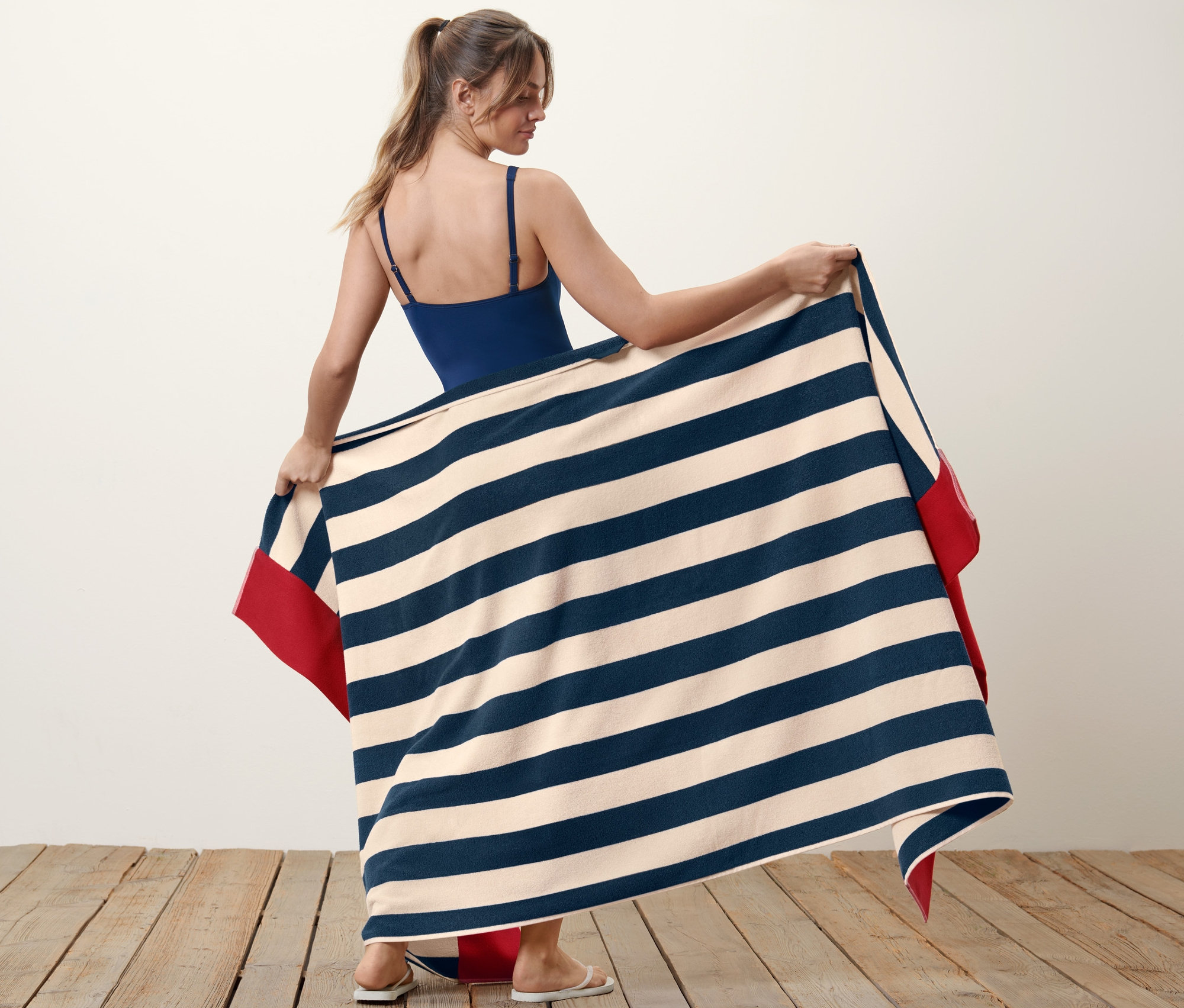 Kadın, mavi ve bej şeritli, kırmızı kenarlı Ekstra Büyük Banyo Havlusu tutuyor.