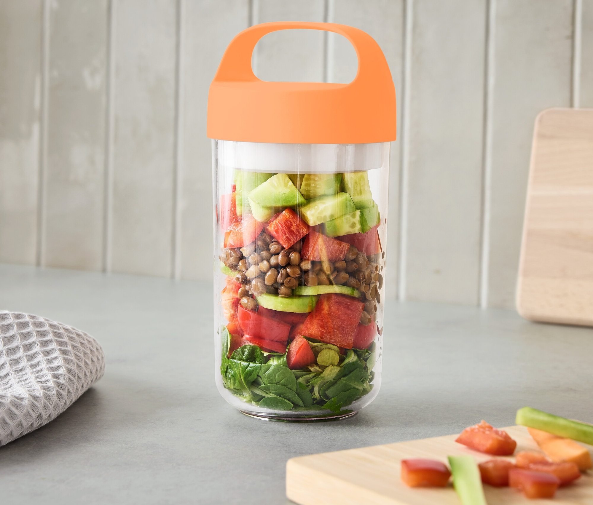 Sebzelerle dolu, kulplu, büyük boy kap, tezgah üzerinde duruyor.