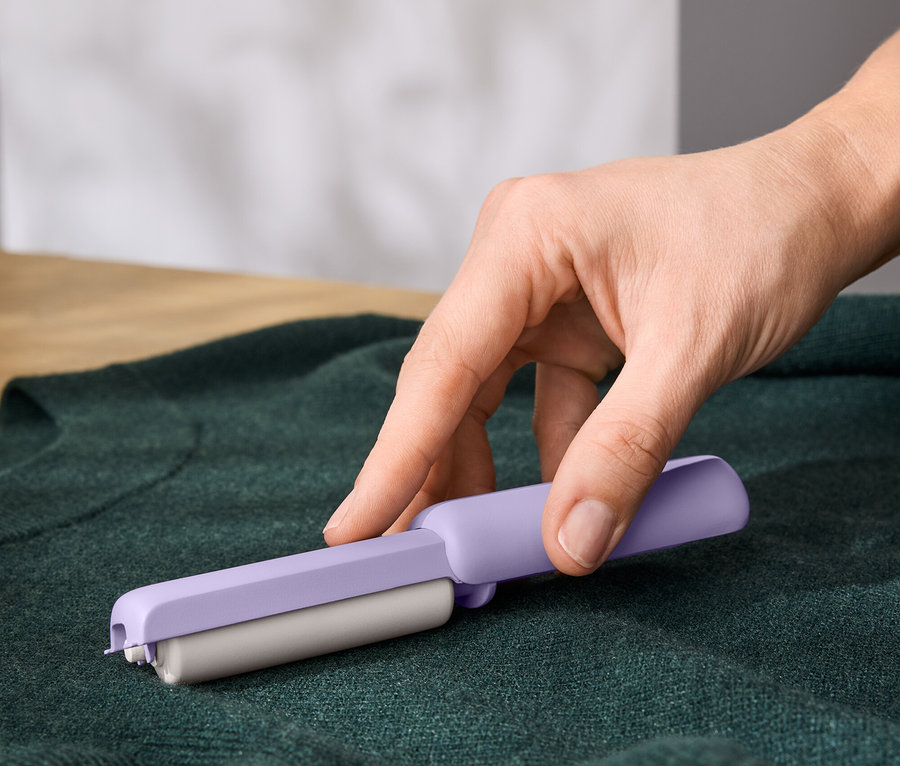 Bir el, yeşil bir kazağın üzerinde mor bir tüy toplayıcı kullanıyor.