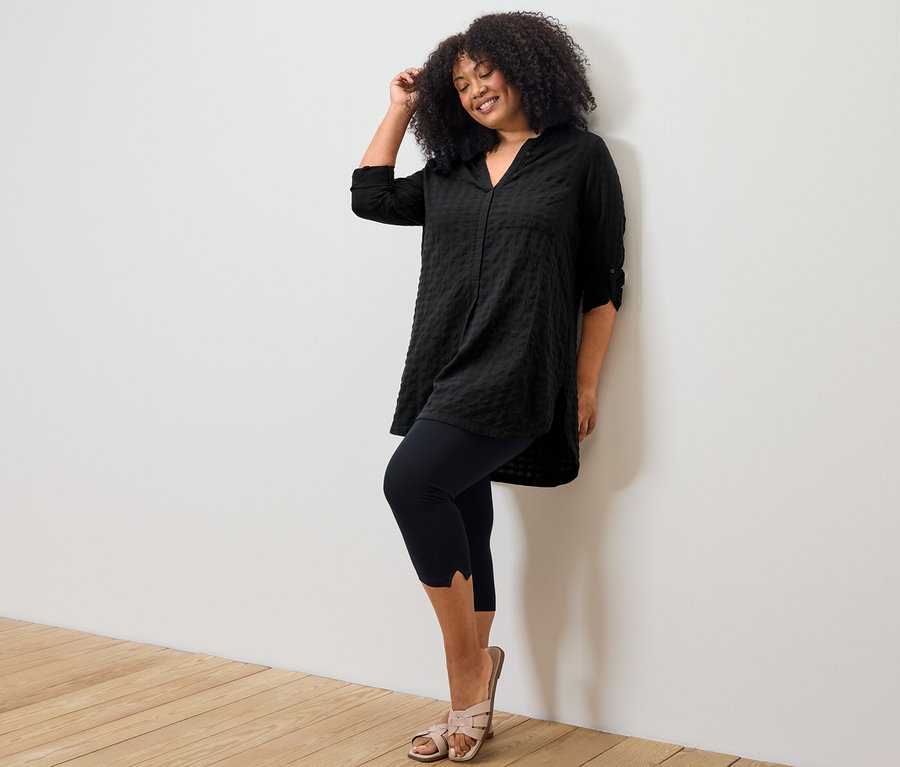 Kadın, siyah dokuma dokulu uzun tunik ve detaylı 3/4 taytla poz veriyor.