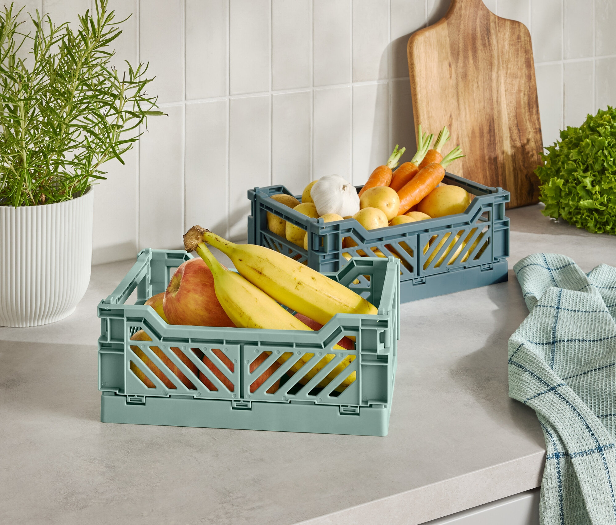 Mutfak tezgahında meyve ve sebzelerle dolu iki plastik sepet.