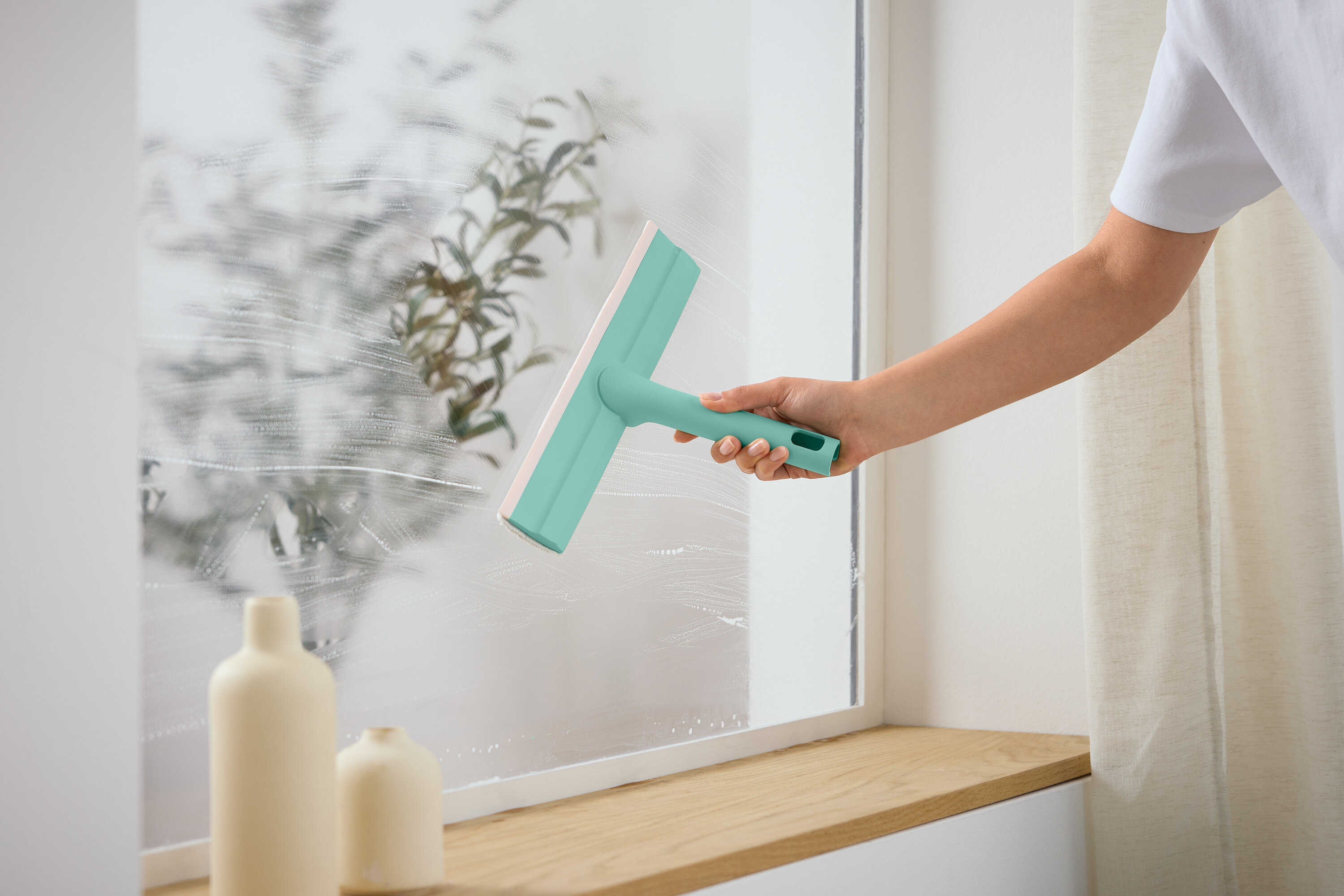 Bir kişi bir pencereyi cam sileceği ile temizliyor.