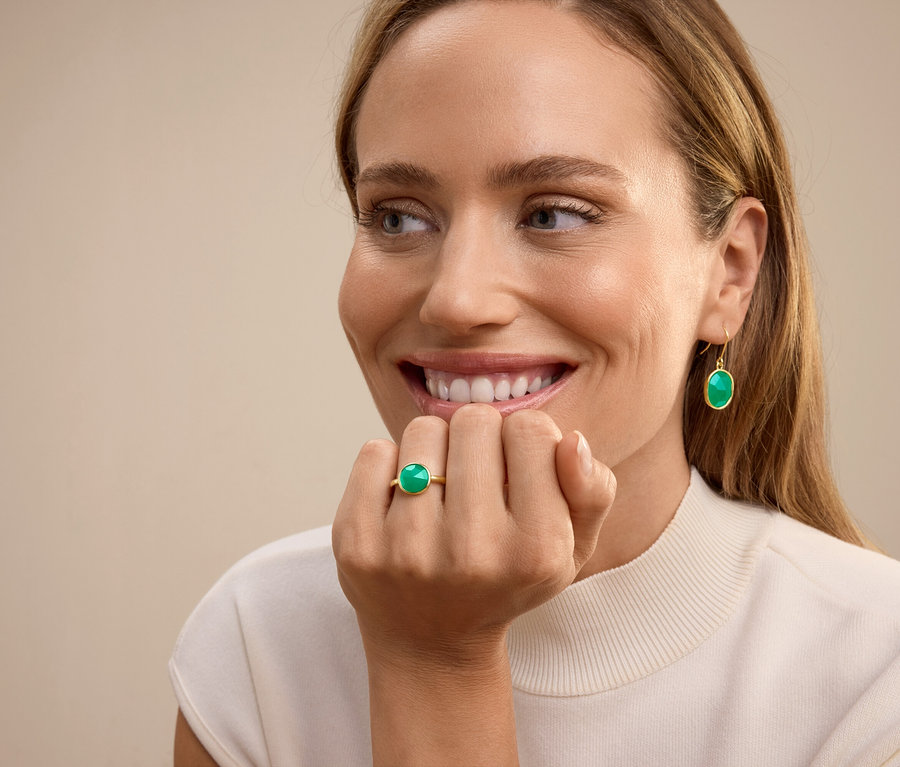 Yüzük parmağında yeşil taşlı yüzük ve kulaklarında yeşil taşlı sallantılı küpeler olan gülümseyen kadın.