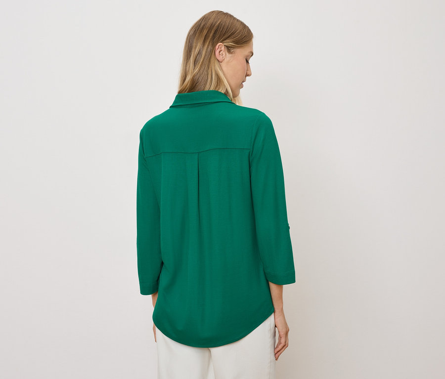 Sırtı kameraya dönük bir kadın yeşil bir gömlek ve beyaz bir pantolon giyiyor.