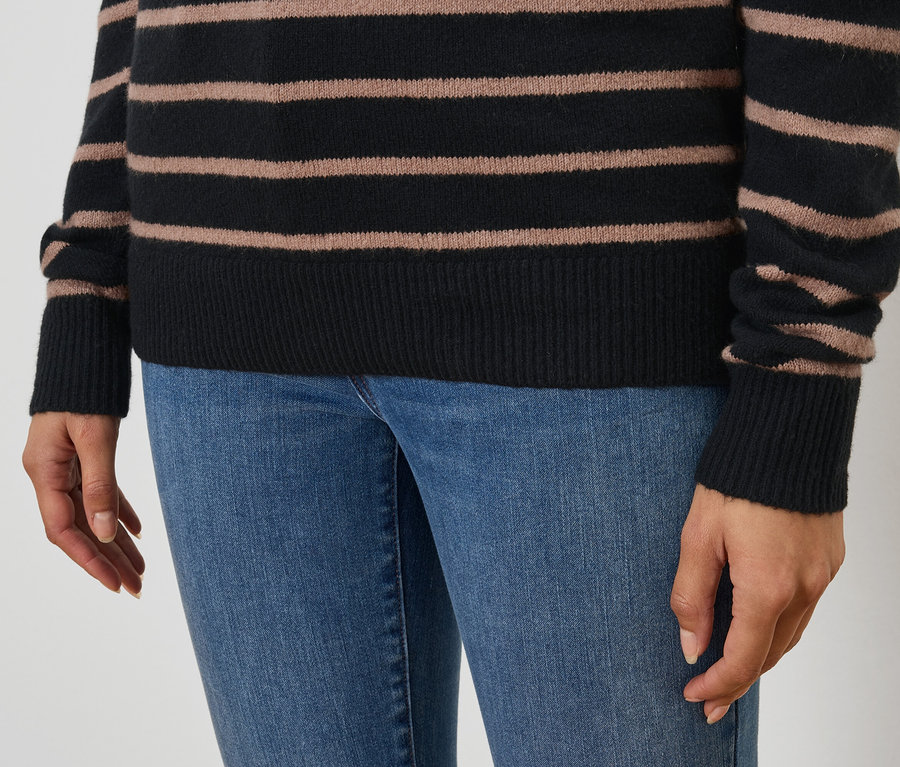 Siyah ve kahverengi çizgili bir kazak ve mavi kot pantolon giyen bir kadının yakın çekimi.