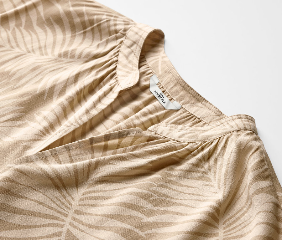 Bej rengi, yaprak baskılı, kısa kollu bir bluzun yakın çekimi.