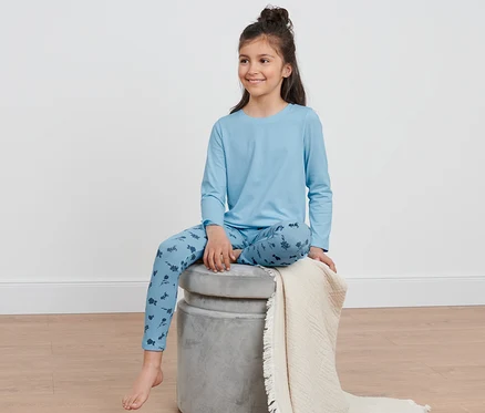 Kız çocuğu mavi çocuk pijama takımıyla bir taburede oturuyor.