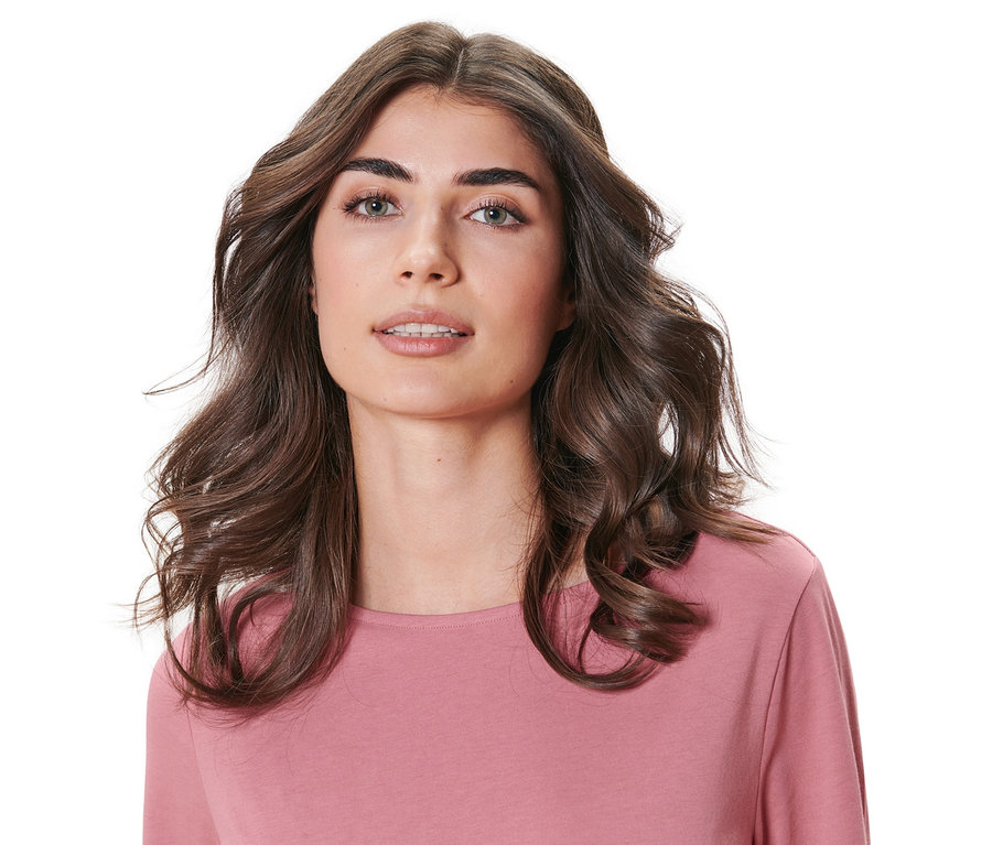 Pembe bir üst giyen dalgalı kahverengi saçlı bir kadının portresi. Saçlar Isısız Saç Şekillendirici ile kıvrılmış.