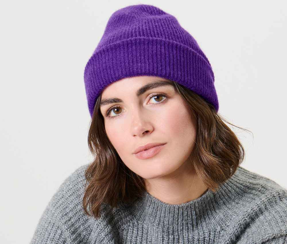 Kadın oturuyor ve mor örgü bere takıyor.