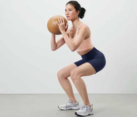 Kadın sağlık topuyla çömelme yapıyor ve kısa spor tayt giyiyor.