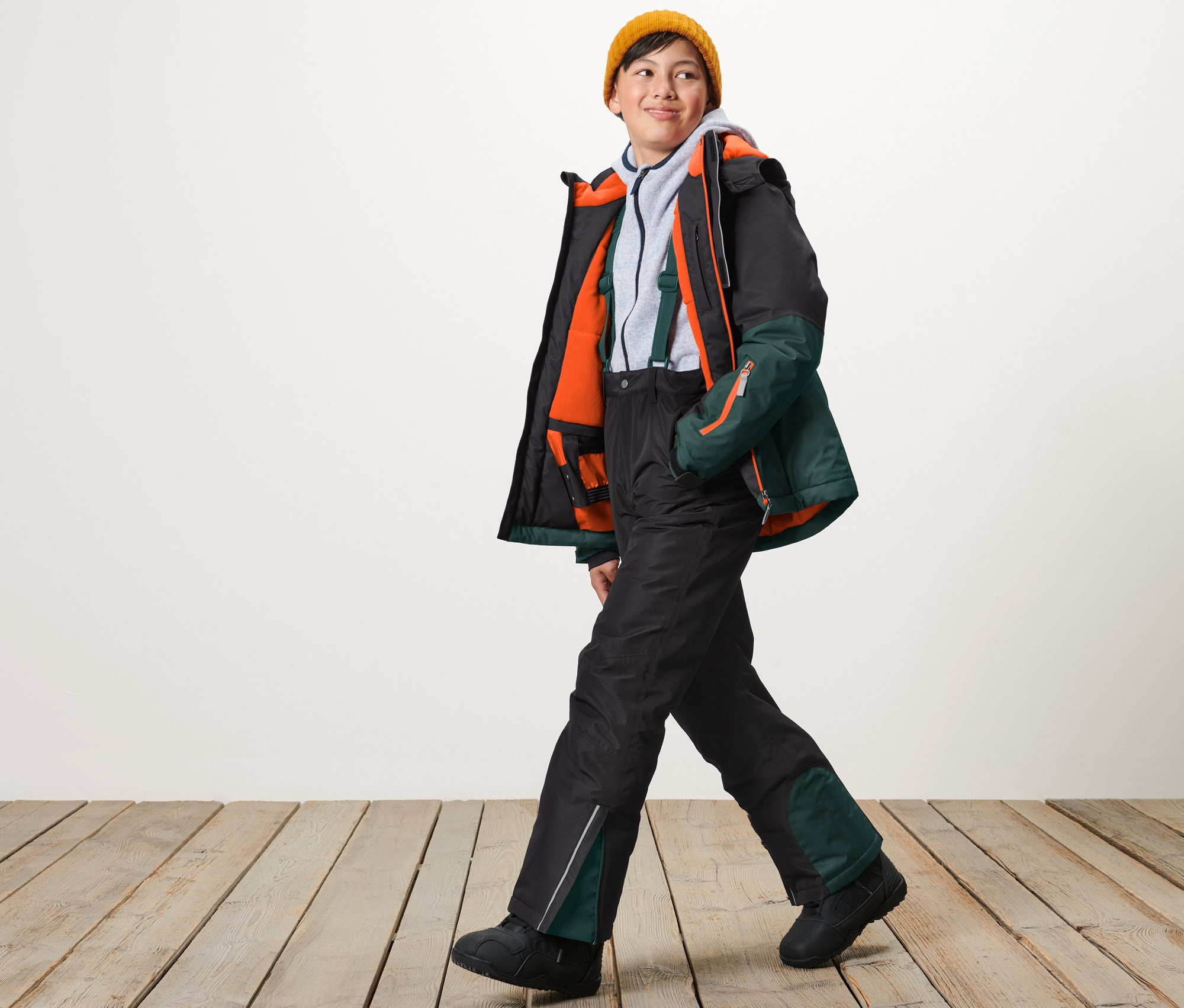 Sarı şapkalı bir çocuk yürüyor ve siyah kayak pantolonu giyiyor.